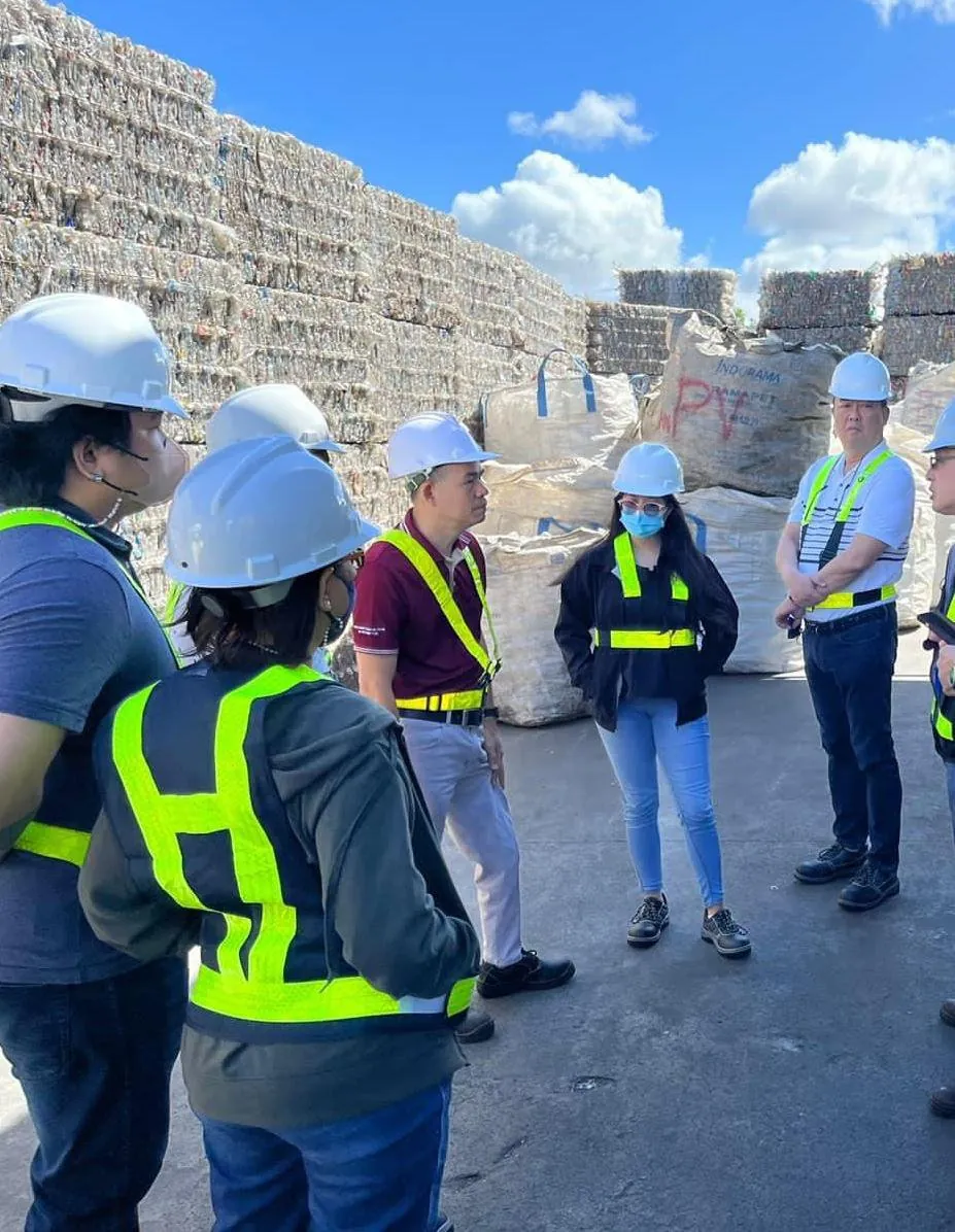 A team in hard hats stands before baled recovered paper at a recycling facility
