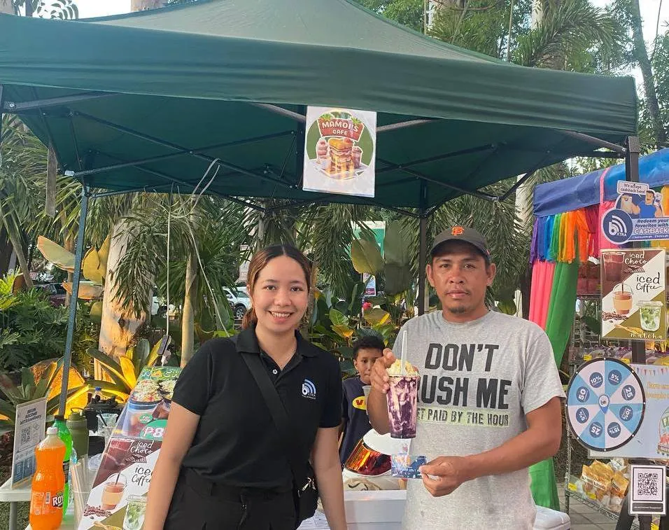 Residents at a Trash to Cashback booth beside a partner-store redemption poster